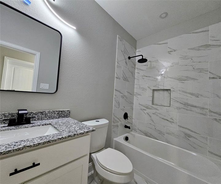 Full bathroom with tiled shower / bath combo, vanity, and toilet