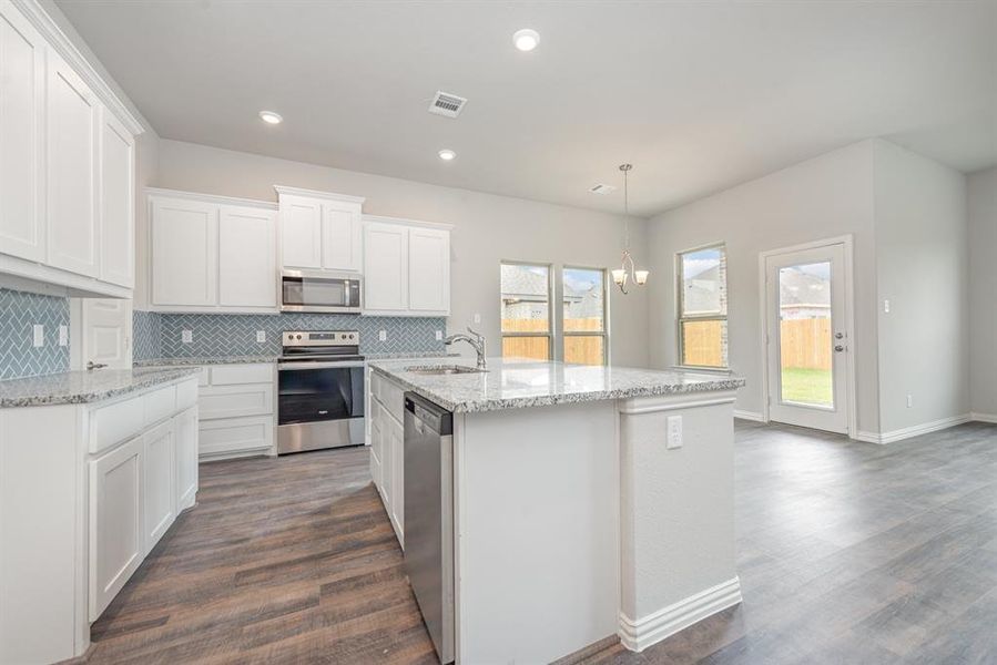 Kitchen with white cabinetry, dark wood-type flooring, an island with sink, hanging light fixtures, and appliances with stainless steel finishes