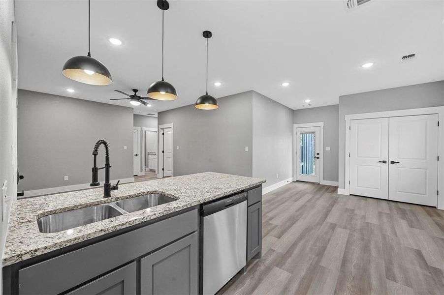 Kitchen with light hardwood / wood-style floors, light stone countertops, ceiling fan, stainless steel dishwasher, and sink