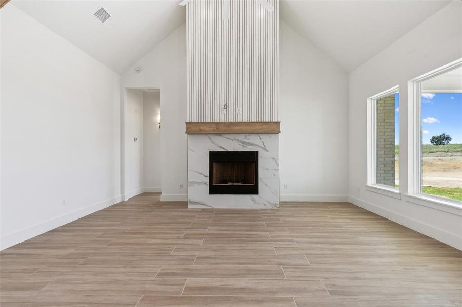 Unfurnished living room with a high end fireplace, high vaulted ceiling, and light hardwood / wood-style flooring