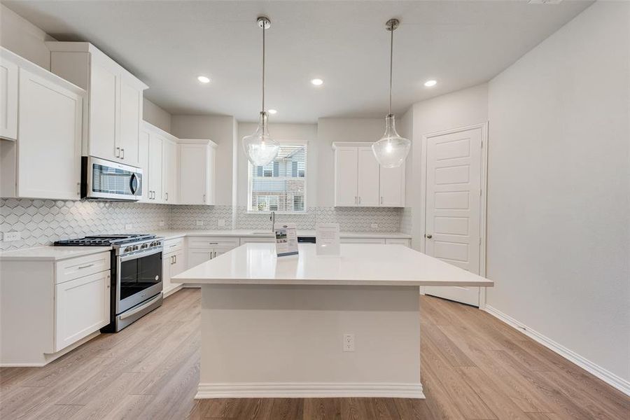 Kitchen featuring tasteful backsplash, white cabinets, a kitchen island, light hardwood / wood-style flooring, and stainless steel appliances