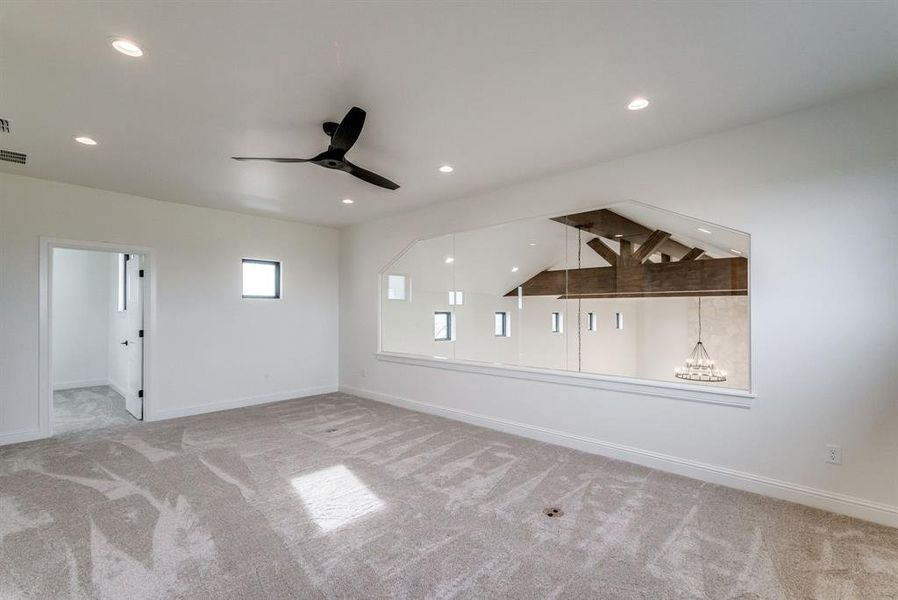 Unfurnished room featuring light colored carpet, ceiling fan with notable chandelier, and lofted ceiling with beams