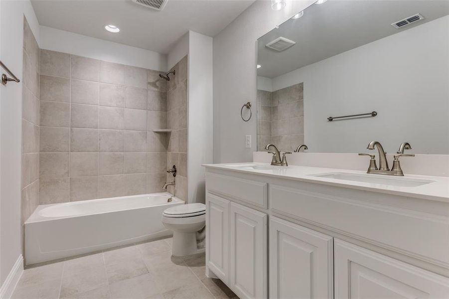 Full bathroom with tile floors, toilet, tiled shower / bath, and double sink vanity