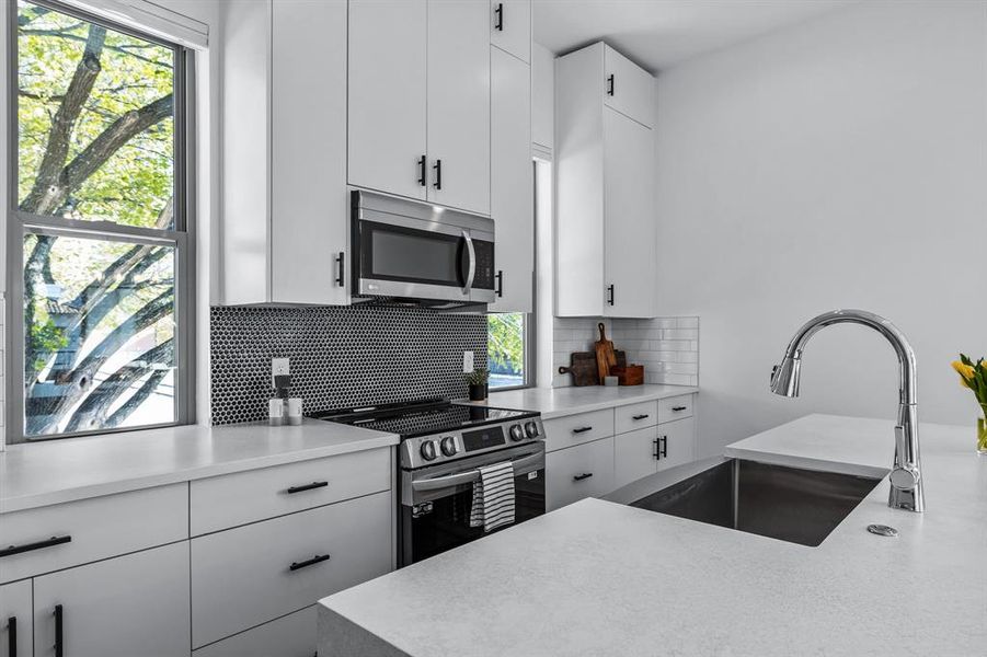 Kitchen with appliances with stainless steel finishes, decorative backsplash, white cabinetry, stainless steel sink