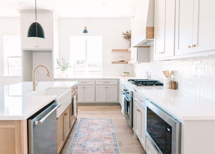 Kitchen featuring custom range hood, white cabinets, pendant lighting, stainless steel appliances, and light hardwood / wood-style flooring