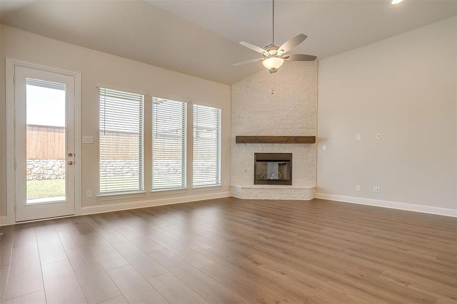 Unfurnished living room with ceiling fan, a stone fireplace, vaulted ceiling, and wood-type flooring