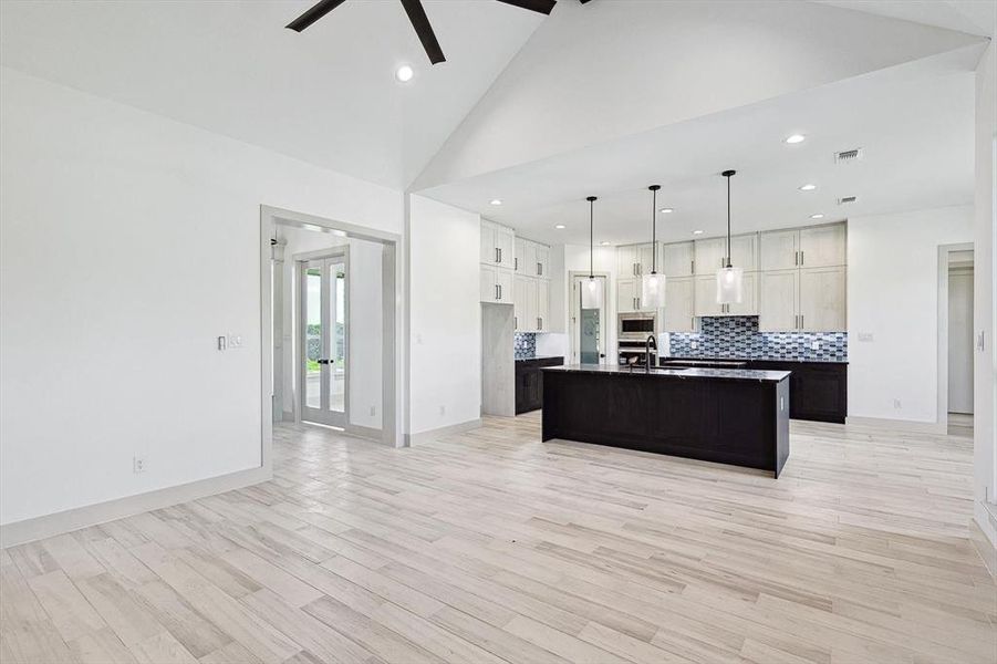 Kitchen featuring a kitchen island with sink, light wood-type flooring, high vaulted ceiling, ceiling fan, and stainless steel microwave