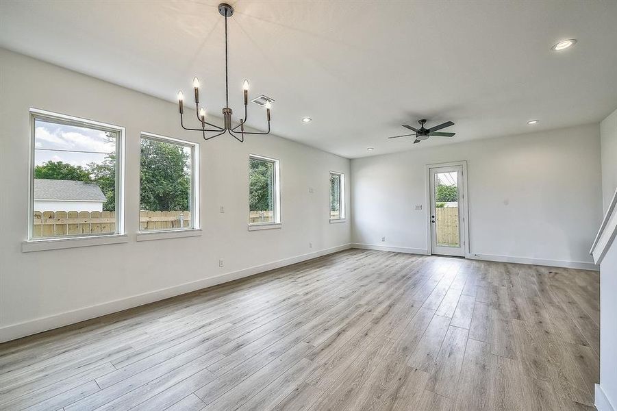 Spare room featuring ceiling fan with notable chandelier and light hardwood / wood-style flooring