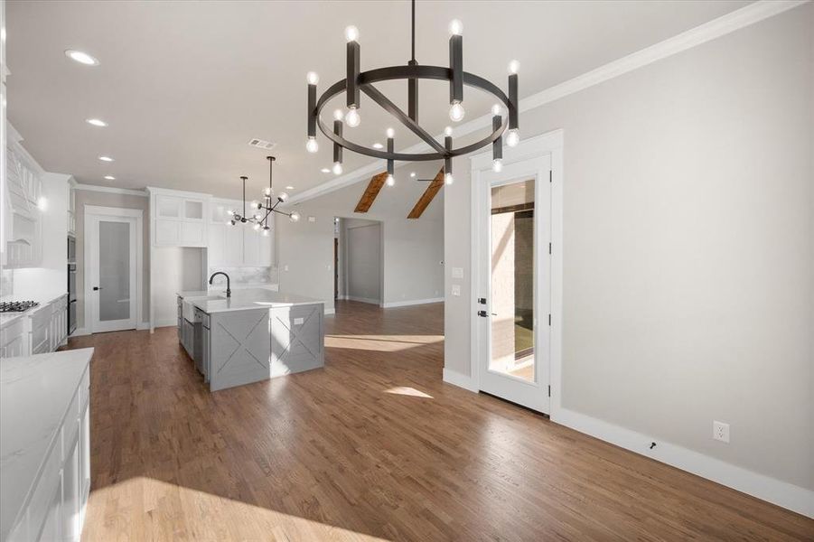 Kitchen featuring dark hardwood / wood-style flooring, hanging light fixtures, white cabinetry, a notable chandelier, and a center island with sink