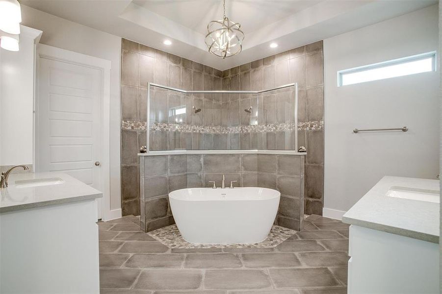 Bathroom with a raised ceiling, separate shower and tub, vanity, and tile walls