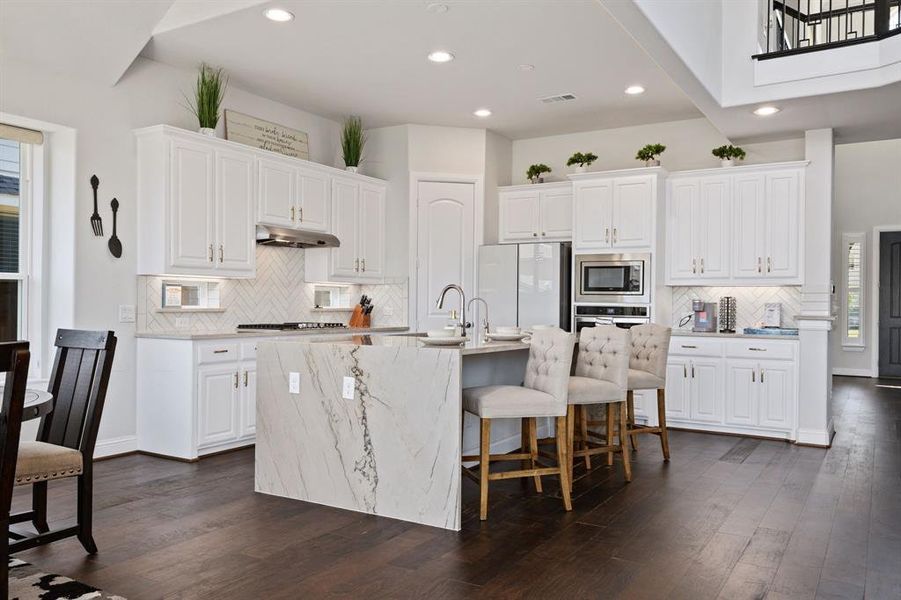 Kitchen with appliances with stainless steel finishes, white cabinets, a kitchen island with sink, and dark hardwood / wood-style floors