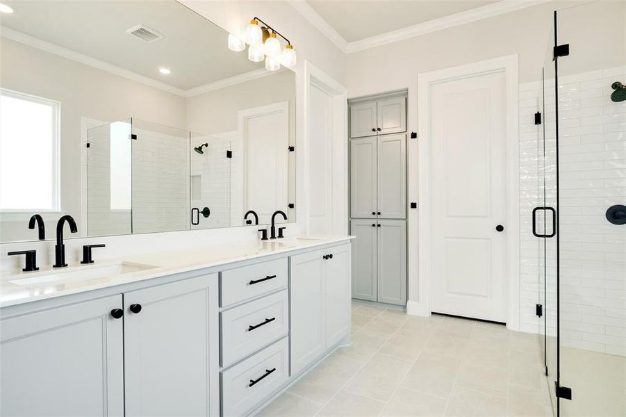 Bathroom featuring tile patterned floors, dual vanity, a shower with shower door, and crown molding