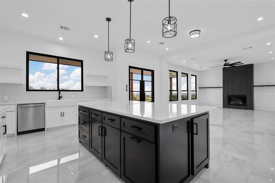 Kitchen with light tile patterned flooring, white cabinets, a kitchen island, stainless steel dishwasher, and a fireplace