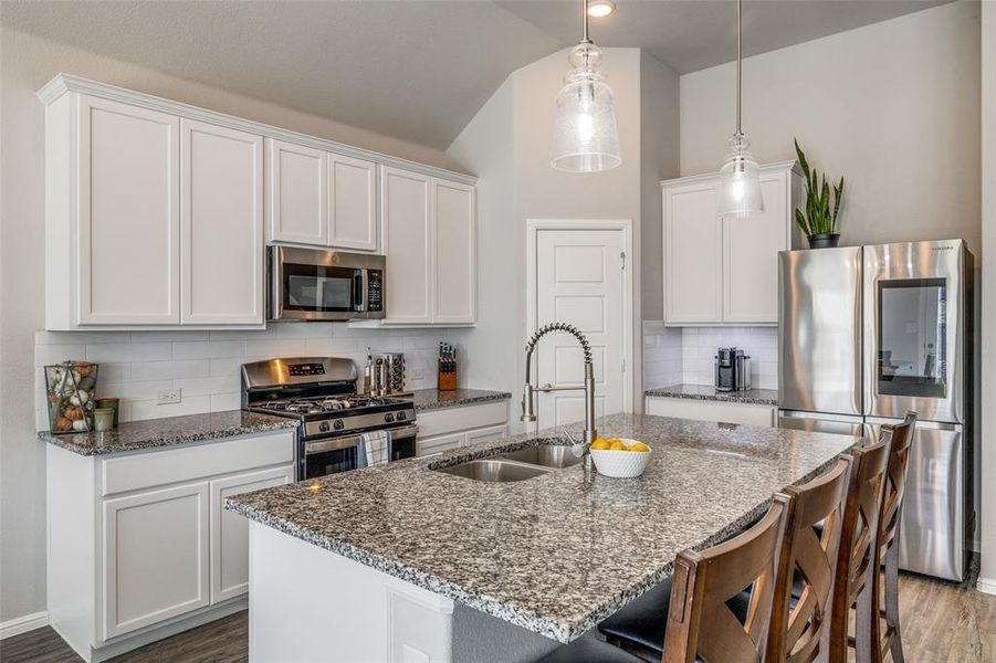 Kitchen featuring pendant lighting, sink, white cabinetry, backsplash, and appliances with stainless steel finishes