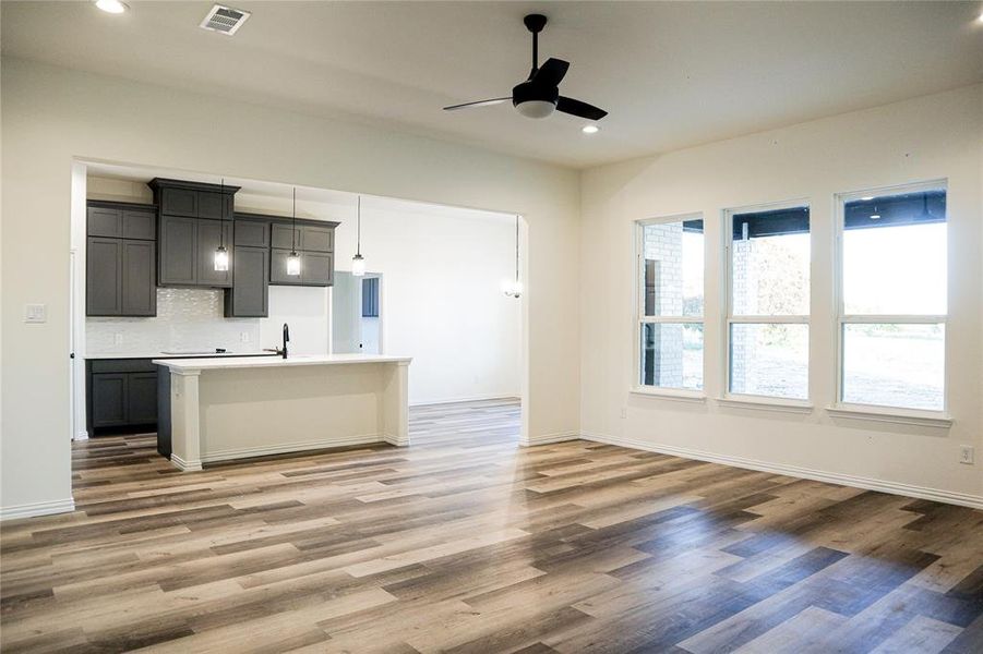 Kitchen with an island with sink, decorative backsplash, decorative light fixtures, hardwood / wood-style floors, and ceiling fan