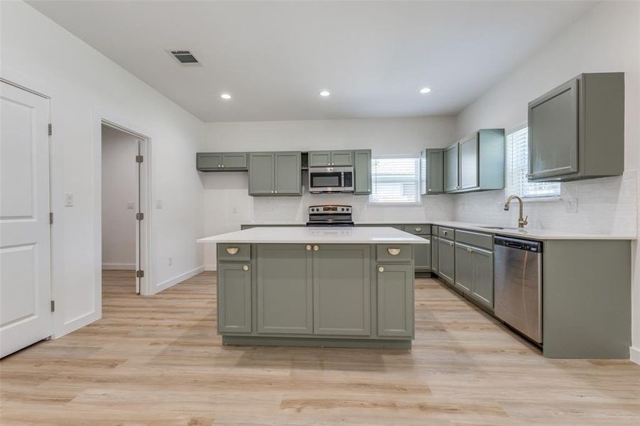 Kitchen with sink, a center island, appliances with stainless steel finishes, light hardwood / wood-style flooring, and backsplash