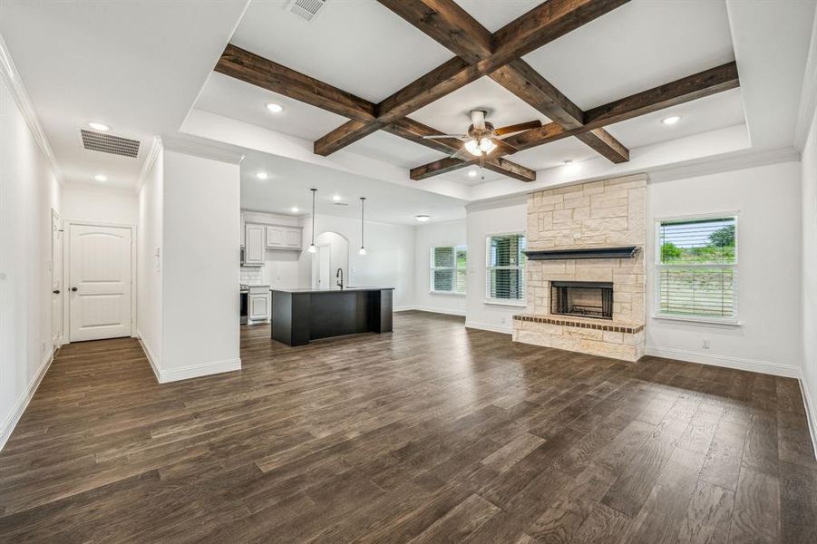 Unfurnished living room featuring a stone fireplace, dark wood-type flooring, ceiling fan, and coffered ceiling