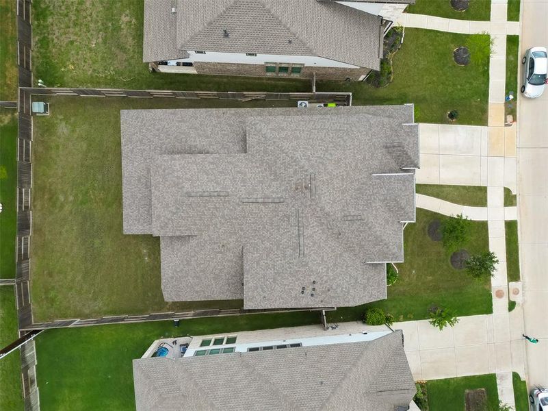 This aerial photo showcases a large, single-family home with a spacious backyard, neatly maintained lawn, and a privacy fence. The property includes a driveway and is located in a well-organized neighborhood with similar homes and manicured landscaping.