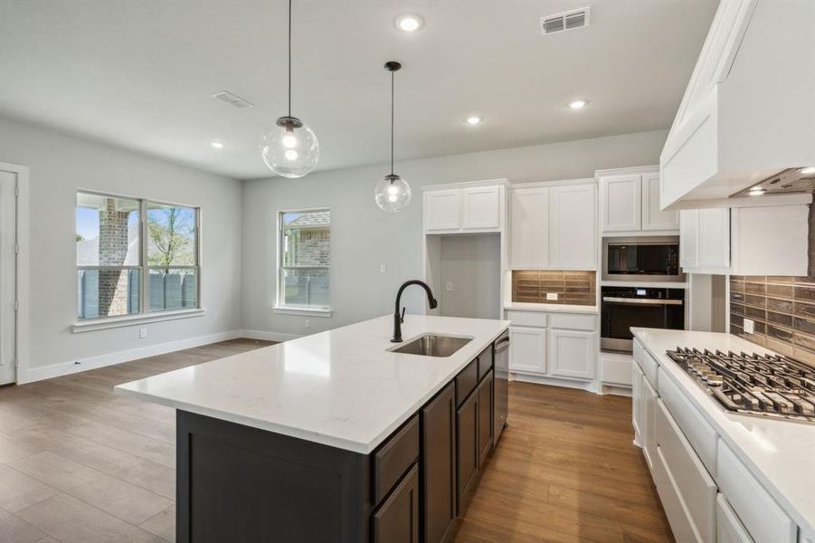 Kitchen featuring appliances with stainless steel finishes, light hardwood / wood-style flooring, decorative light fixtures, and an island with sink