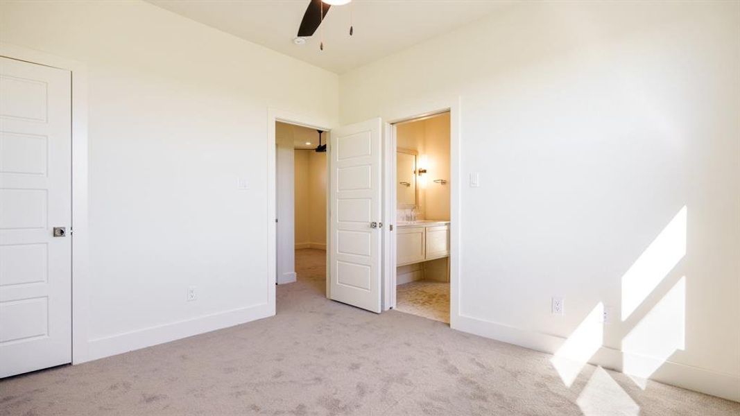 Unfurnished bedroom featuring light colored carpet, connected bathroom, and ceiling fan