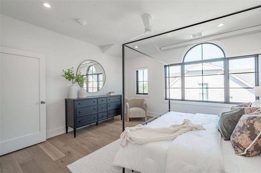 Primary bedroom featuring ceiling fan and light hardwood flooring, Pella windows, and automatic shades