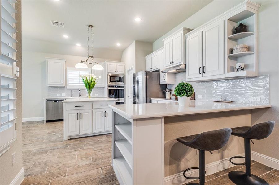 Kitchen featuring a breakfast bar, tasteful backsplash, white cabinets, appliances with stainless steel finishes, and decorative light fixtures