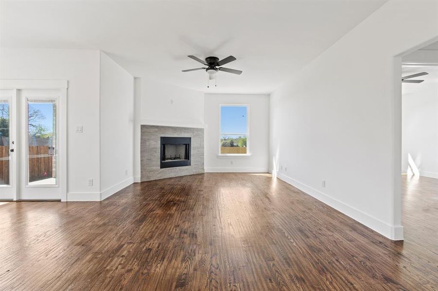 Unfurnished living room with dark wood-type flooring, ceiling fan, and a tiled fireplace