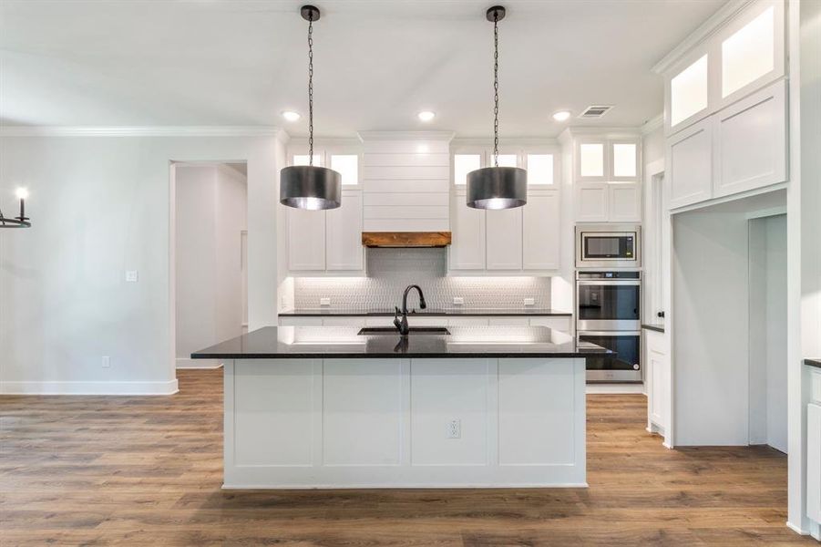 Kitchen with white cabinetry, wood-type flooring, stainless steel appliances, an island with sink, and sink