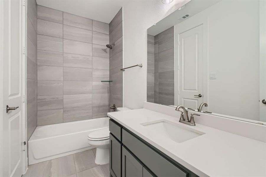 Full bathroom featuring vanity, tiled shower / bath combo, toilet, and tile patterned flooring