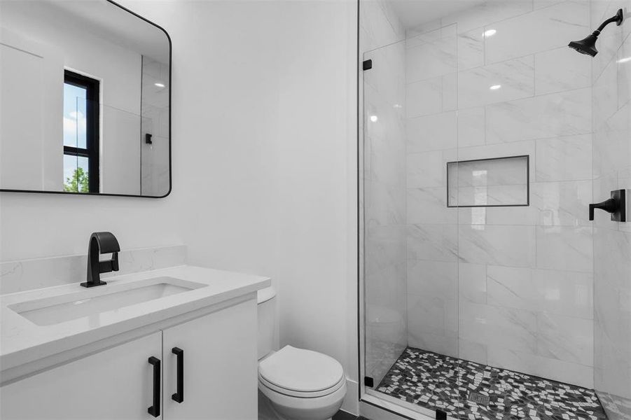 Bathroom featuring tiled shower, toilet, and vanity