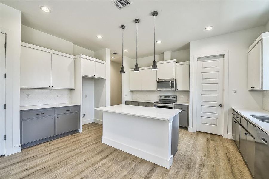 Kitchen with white cabinets, hanging light fixtures, appliances with stainless steel finishes, light hardwood / wood-style floors, and a kitchen island