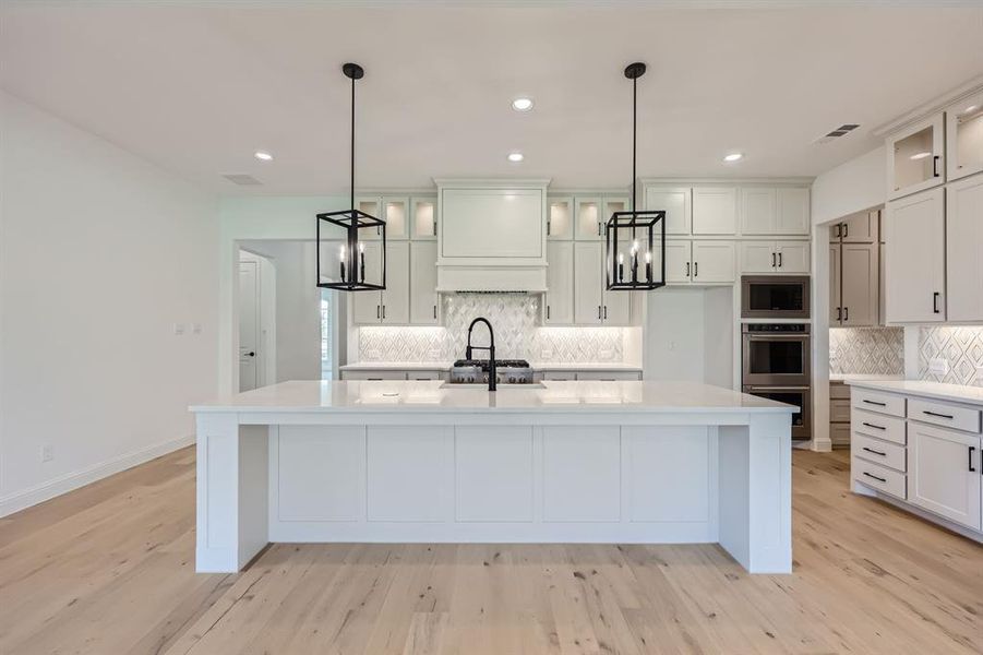 Kitchen with an island with sink, decorative light fixtures, and light wood-type flooring