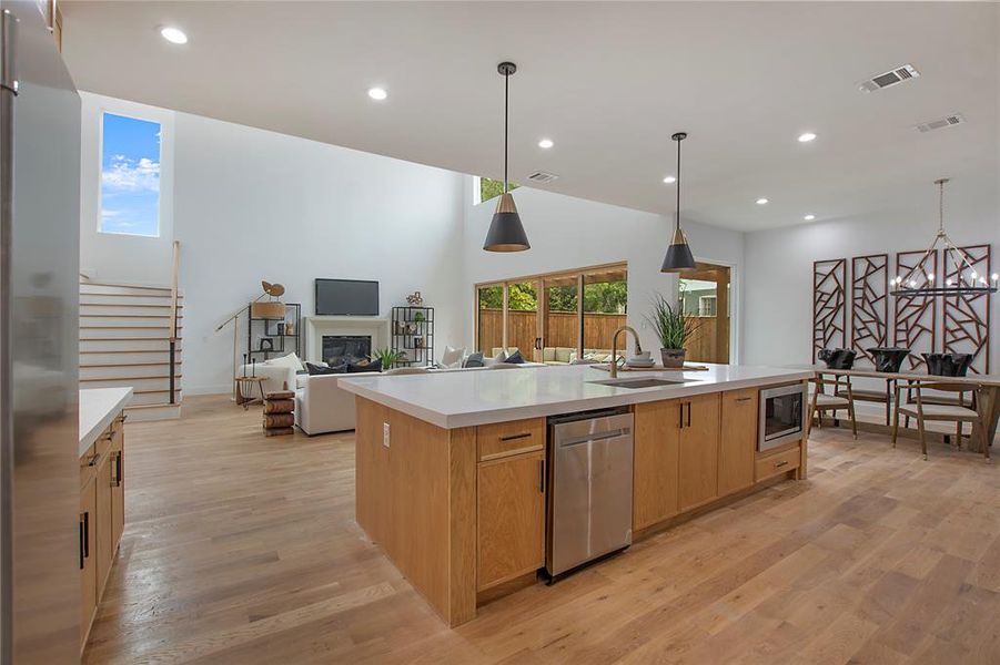 Kitchen with light wood-type flooring, pendant lighting, sink, appliances with stainless steel finishes, and a center island with sink