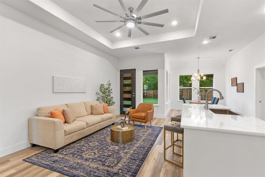 Living room featuring ceiling fan with notable chandelier, light hardwood / wood-style flooring, a raised ceiling, and sink