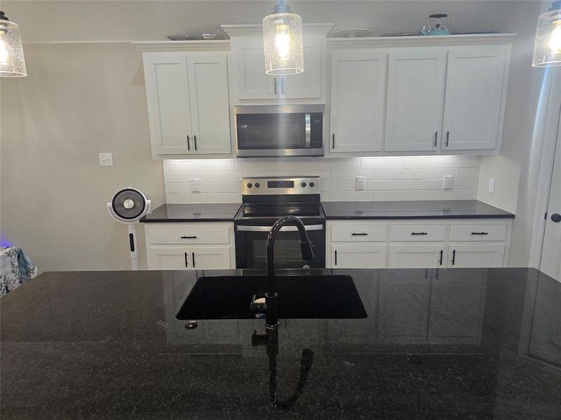 Kitchen with appliances with stainless steel finishes, hanging light fixtures, white cabinetry, tasteful backsplash, and sink