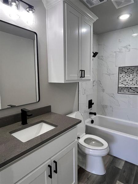 Full bathroom with wood-type flooring, vanity, tiled shower / bath combo, and toilet