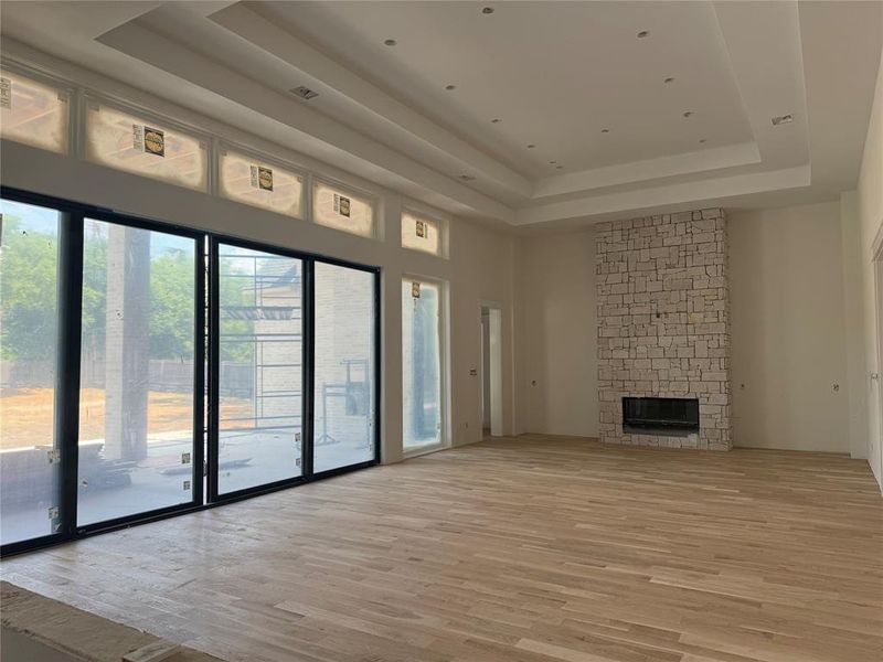 Unfurnished living room featuring a stone fireplace, light hardwood / wood-style flooring, and a raised ceiling