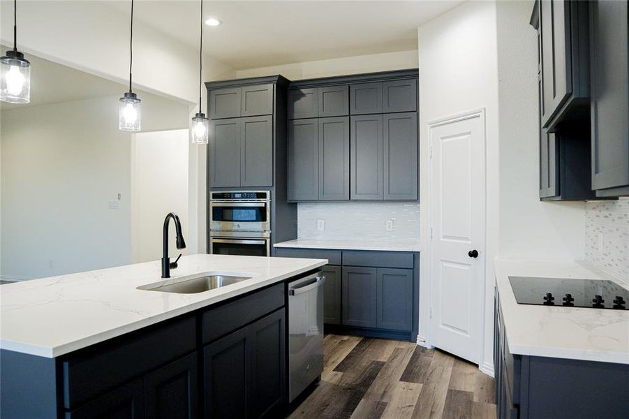 Kitchen featuring dark wood-type flooring, sink, hanging light fixtures, decorative backsplash, and appliances with stainless steel finishes