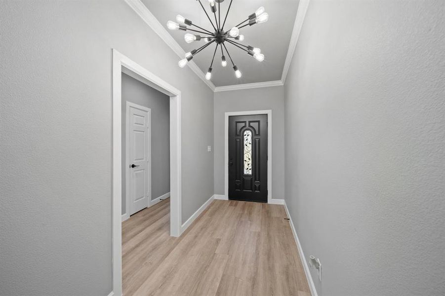 Entrance foyer featuring ornamental molding, a notable chandelier, and light wood-type flooring