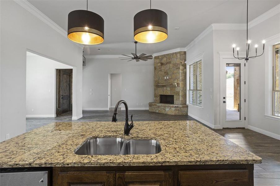 Kitchen featuring ornamental molding, decorative light fixtures, a fireplace, and a center island with sink