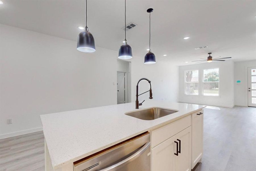 Kitchen featuring stainless steel dishwasher, hanging light fixtures, sink, a center island with sink, and light hardwood / wood-style flooring