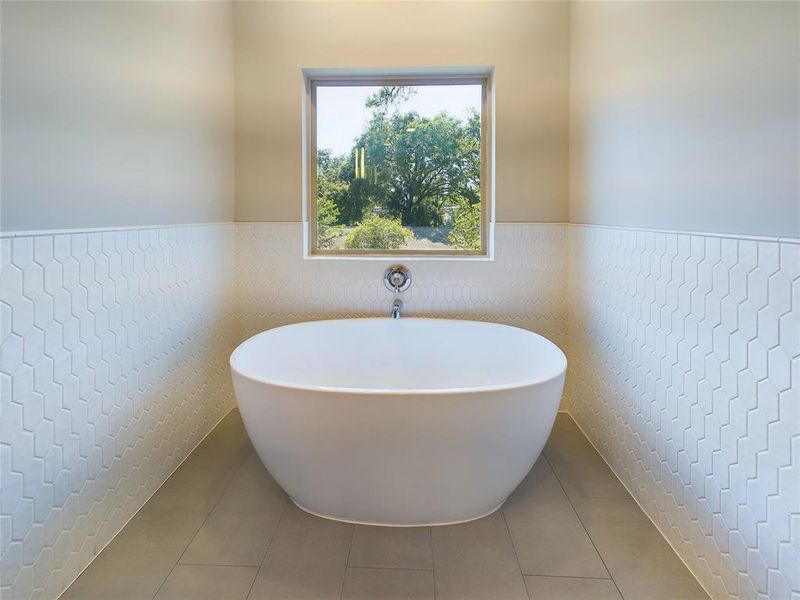 Freestanding bathtub and window allowing natural light in primary bathroom.
