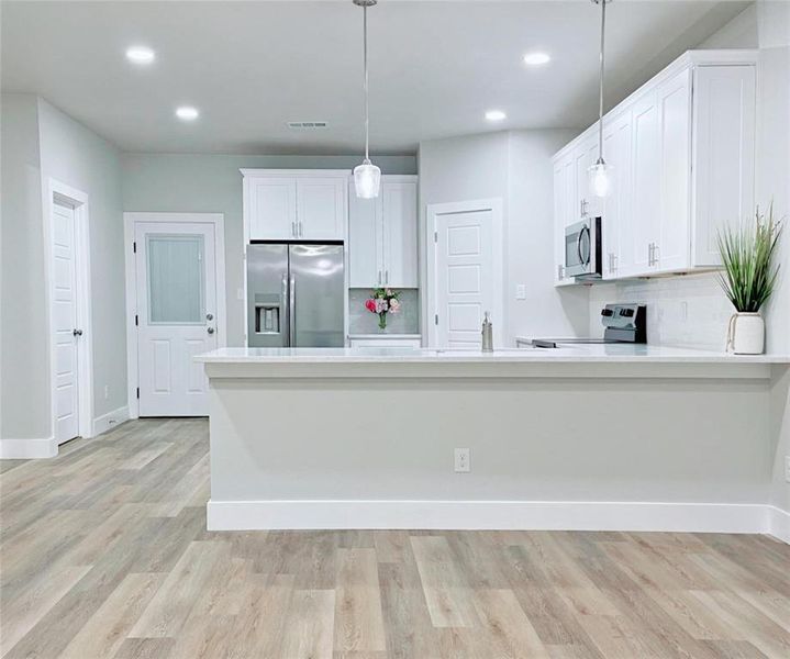 Kitchen featuring white cabinets, hanging light fixtures, tasteful backsplash, stainless steel appliances, and light hardwood / wood-style floors