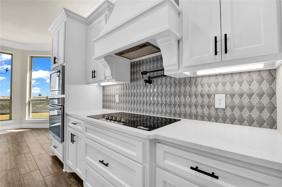 Kitchen with black electric stovetop, custom range hood, tasteful backsplash, and white cabinets