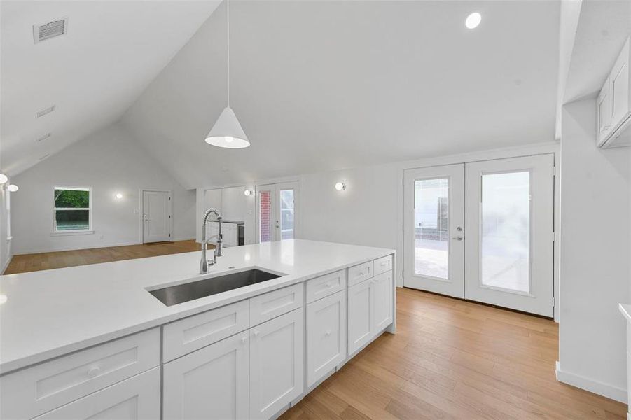 Kitchen with white cabinets, sink, vaulted ceiling, light hardwood / wood-style flooring, and decorative light fixtures