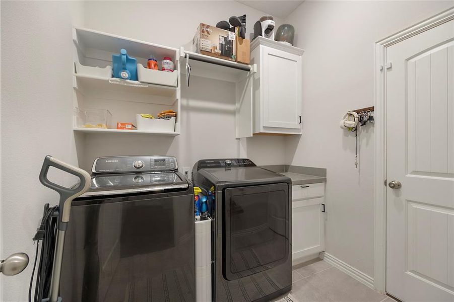 Clothes washing area with cabinets, washing machine and clothes dryer, and light tile patterned floors