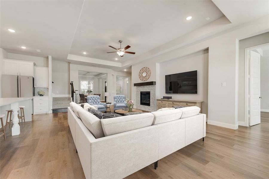 Living room with light wood-type flooring, ceiling fan, and a raised ceiling