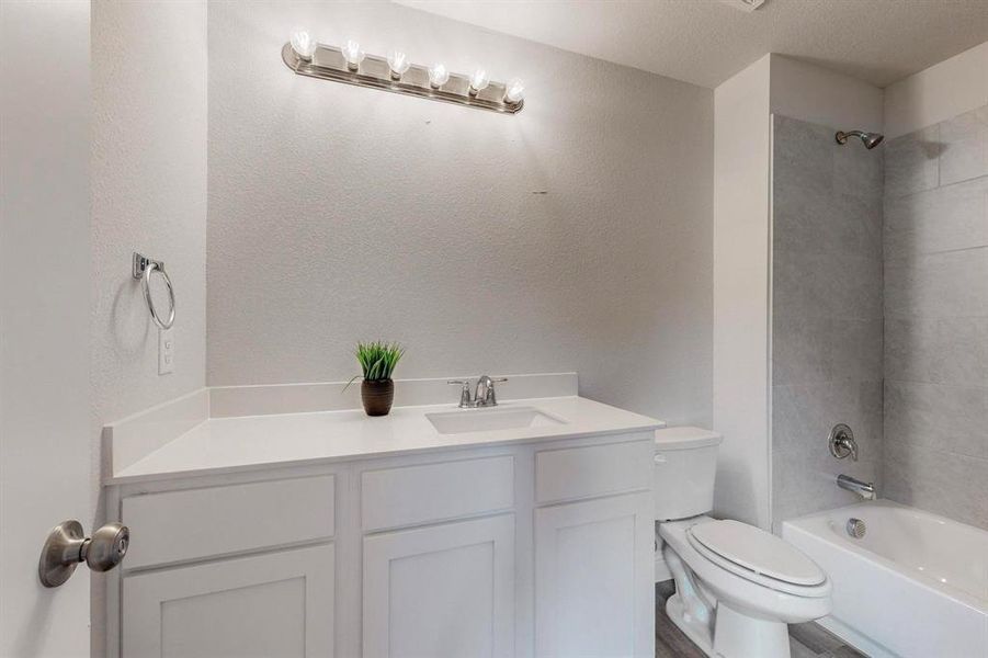 Full bathroom with tiled shower / bath, vanity, toilet, and a textured ceiling