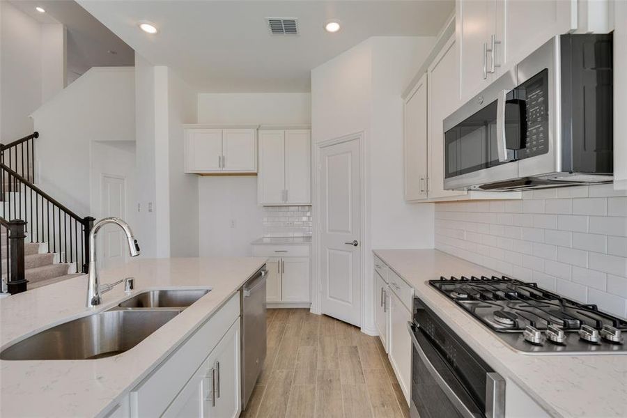 Kitchen with appliances with stainless steel finishes, sink, light hardwood / wood-style floors, decorative backsplash, and white cabinetry