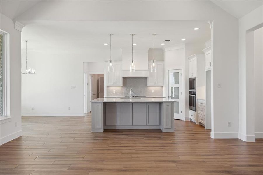 Kitchen featuring white cabinetry, light wood-type flooring, a center island with sink, and oven